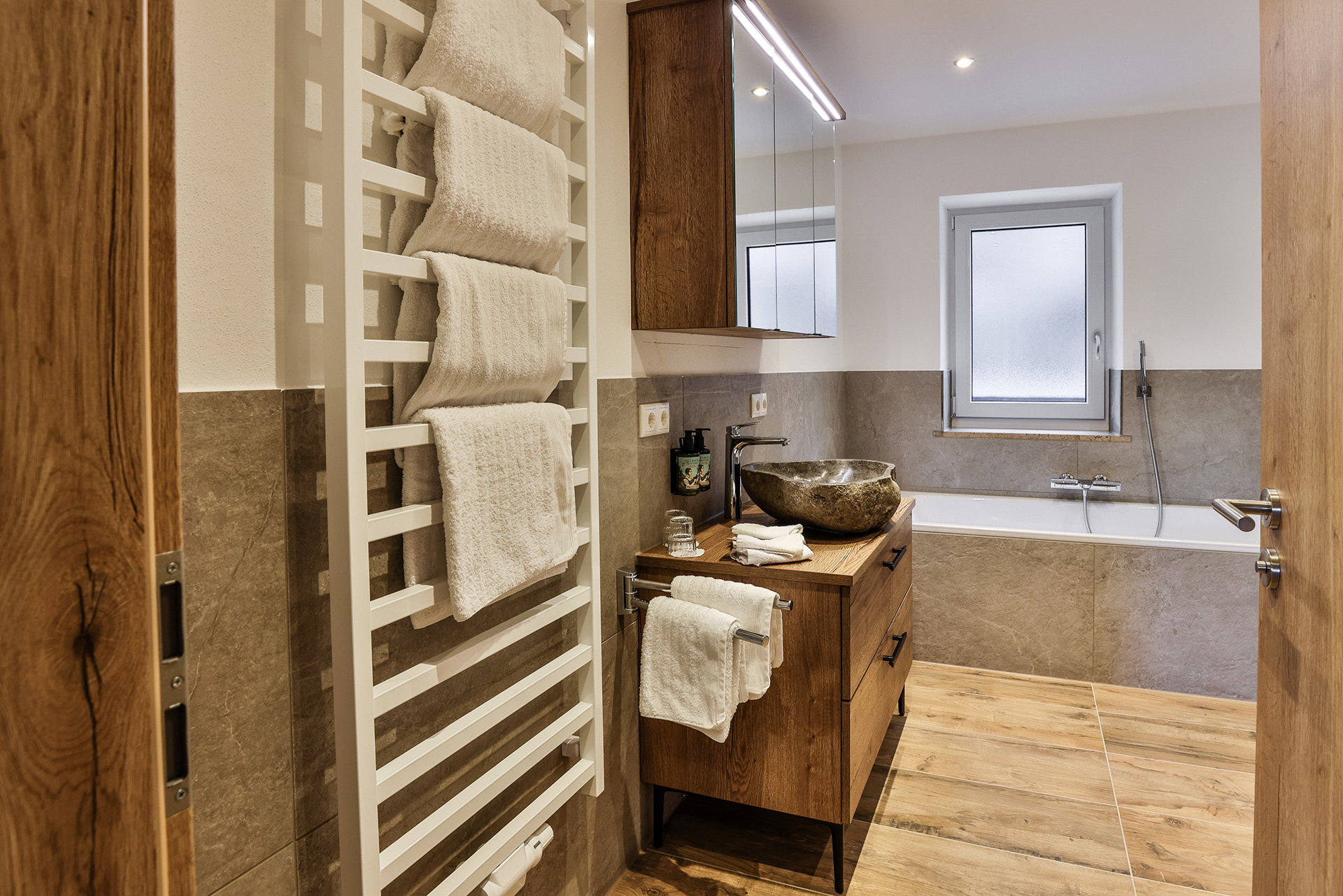 Im modernen Badezimmer erwartet Sie ein großzügiger Duschbereich sowie eine Badewanne und ein Naturstein-Waschbecken für den besonderen Alpenflair.